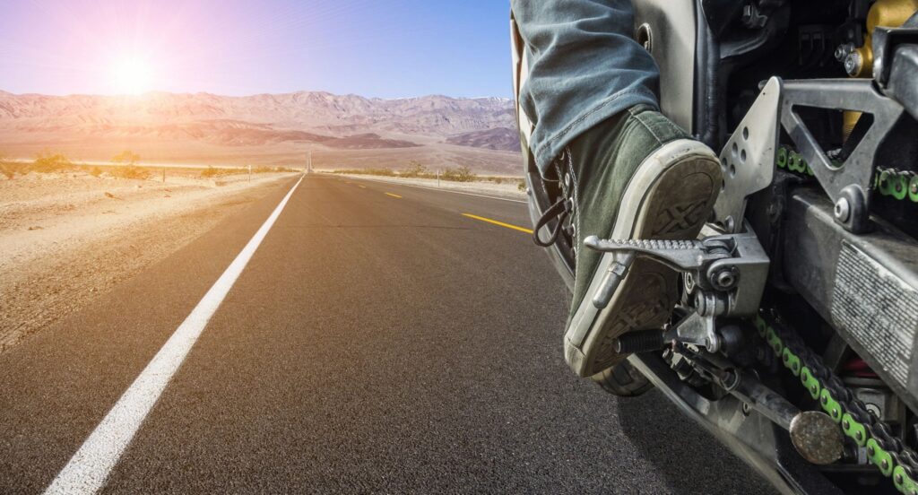 Milford Motorcycle accident lawyer features photo of the foot and pedal of a motorcylist driving down new hampshire road toward sunrise, by milford personal injury law firm 